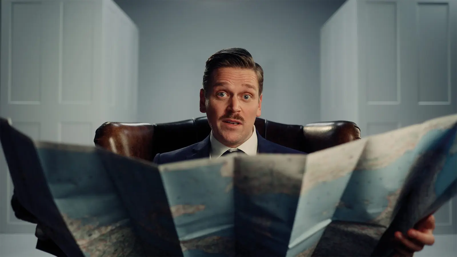 Still: man in een leren stoel achter een opengevouwen kaart